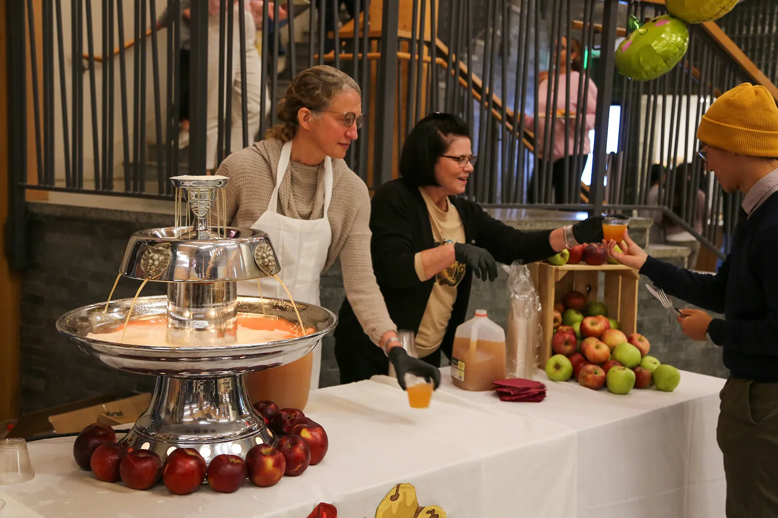 Dining services members serve apple cider from fountain to students during local harvest dinner.