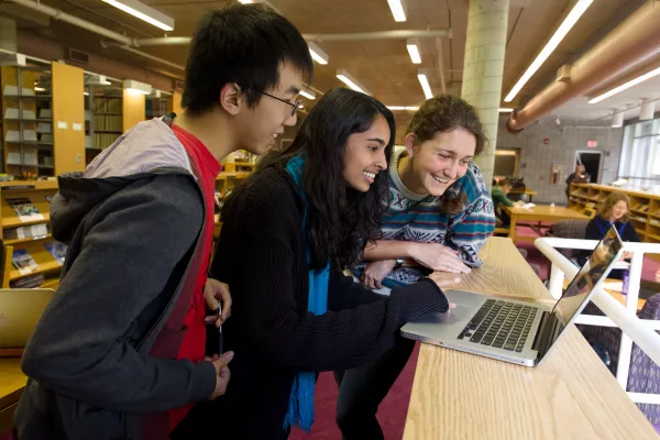 3 students looking at a Mac laptop in the library